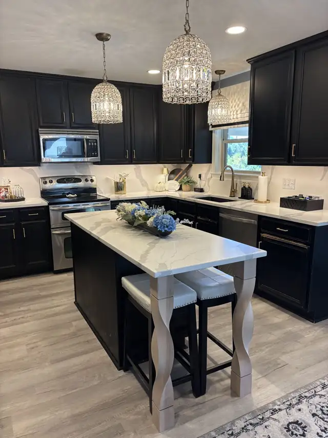 Kitchen with black shaker cabinets, stainless appliances and a white stone island with seating