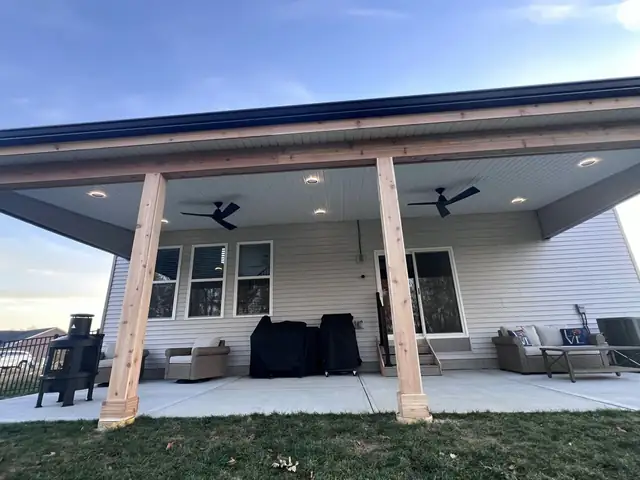 New covered patio with wood-wrapped posts, recessed lights and a concrete pad behind a two-story home