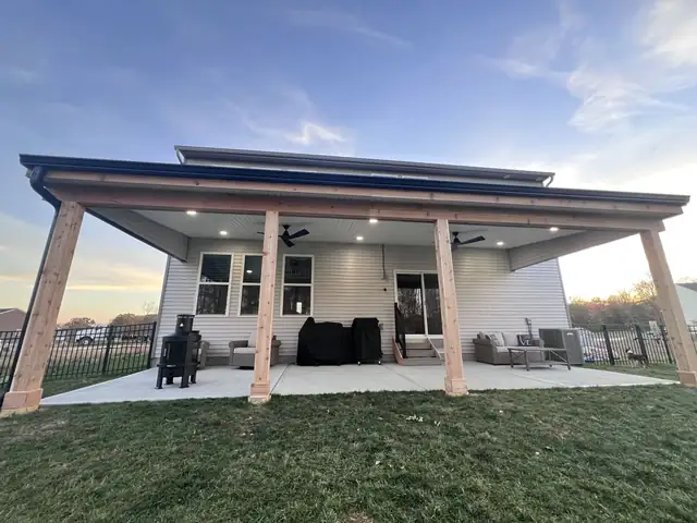 Covered patio at dusk with wood posts and lit ceiling seen from the yard