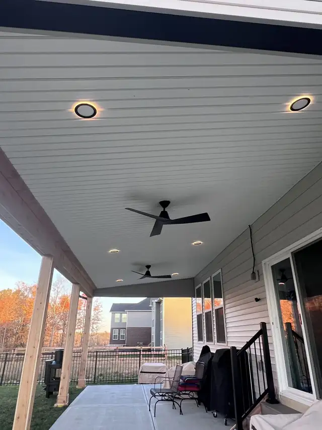 Covered patio ceiling in white planks with recessed lights and two black ceiling fans