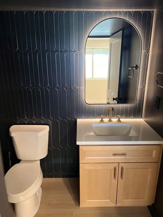 Close view of a brass faucet and vessel-style sink on a light wood vanity against black tile