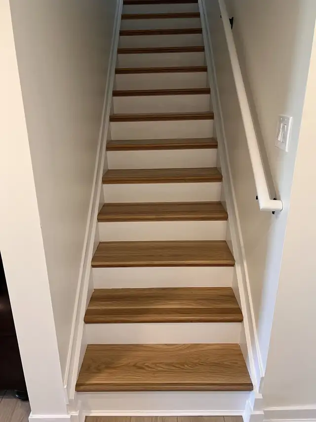 New hardwood stair treads with white risers and a wall-mounted handrail leading to a basement