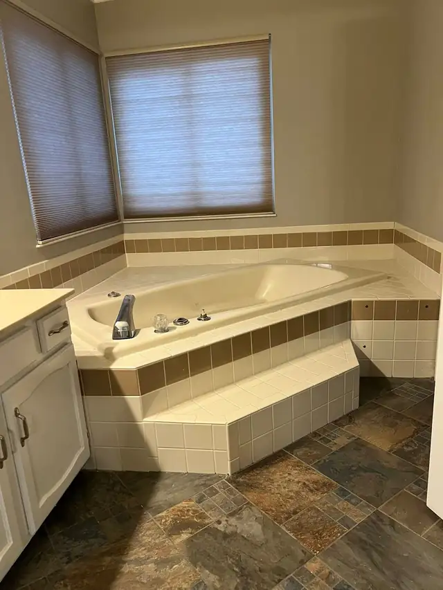 Master bathroom before remodel with tiled corner tub, beige accent tile and dated vanity