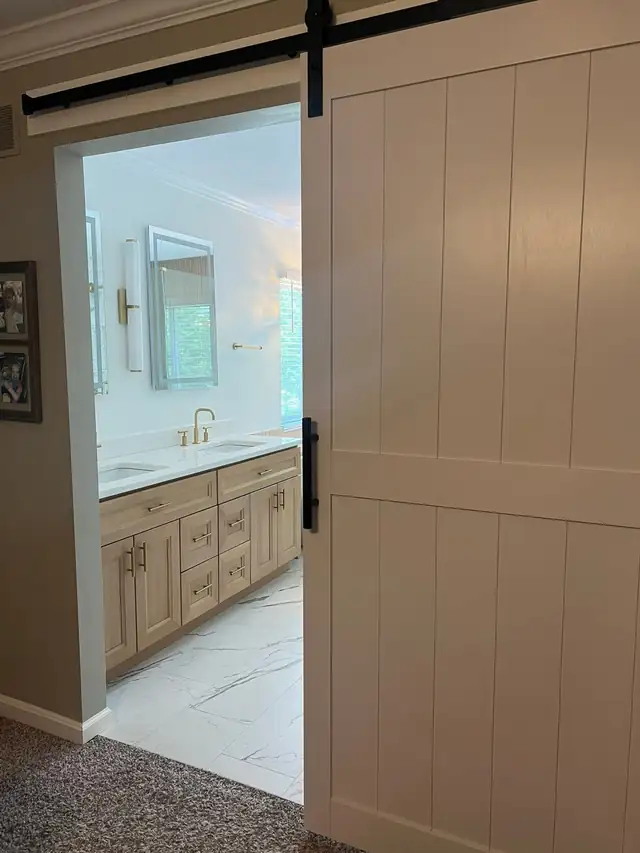 Light wood bathroom vanity with brass fixtures next to a sliding barn door