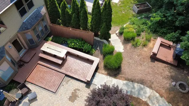 Aerial view of a backyard with a wood deck, paver walkways and evergreen landscaping
